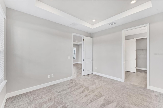 unfurnished bedroom with a closet, a spacious closet, light carpet, and a tray ceiling