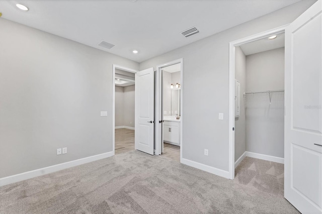 unfurnished bedroom featuring light carpet, a walk in closet, sink, connected bathroom, and a closet