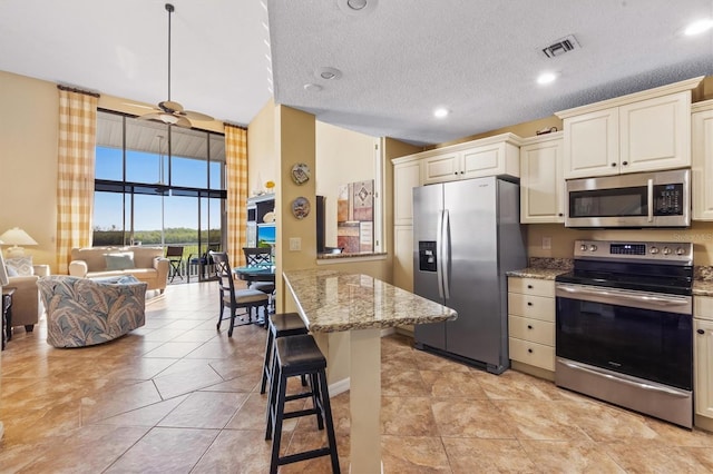 kitchen featuring ceiling fan, a breakfast bar, cream cabinetry, and appliances with stainless steel finishes