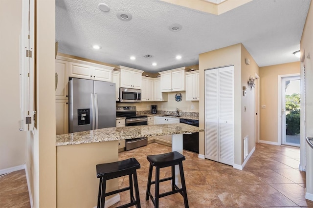 kitchen featuring appliances with stainless steel finishes, light stone counters, a textured ceiling, sink, and a breakfast bar area