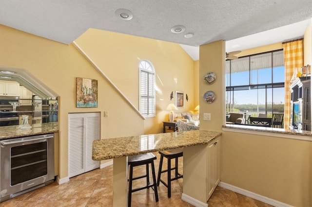 kitchen featuring a kitchen bar, appliances with stainless steel finishes, kitchen peninsula, light stone counters, and wine cooler