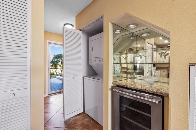 laundry area with wine cooler, dark tile patterned floors, and stacked washer / drying machine