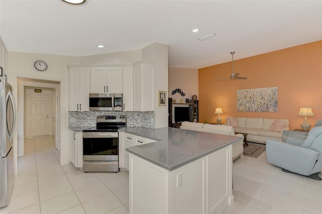 kitchen with kitchen peninsula, appliances with stainless steel finishes, backsplash, light tile patterned floors, and white cabinets