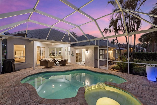 pool at dusk with glass enclosure, a patio area, an outdoor hangout area, and an in ground hot tub