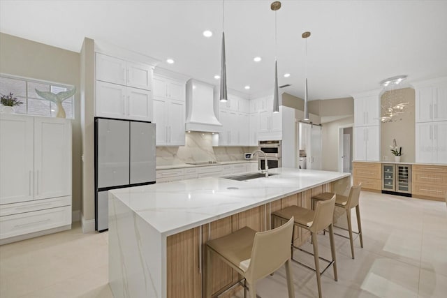 kitchen featuring premium range hood, sink, white cabinets, hanging light fixtures, and a large island