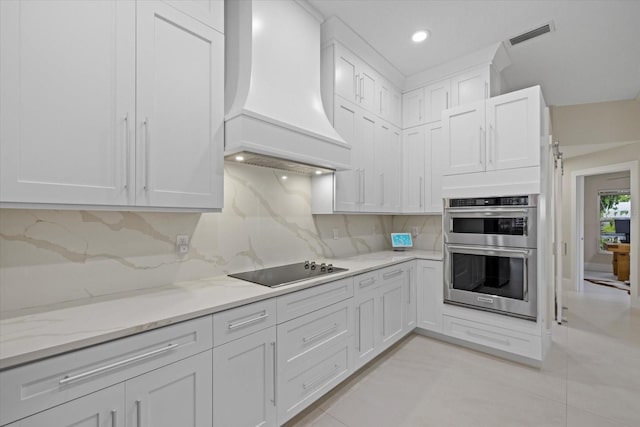 kitchen with white cabinetry, premium range hood, backsplash, double oven, and black electric cooktop