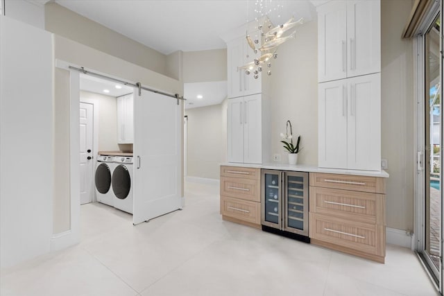 laundry room with cabinets, a barn door, wine cooler, washing machine and dryer, and light tile patterned flooring