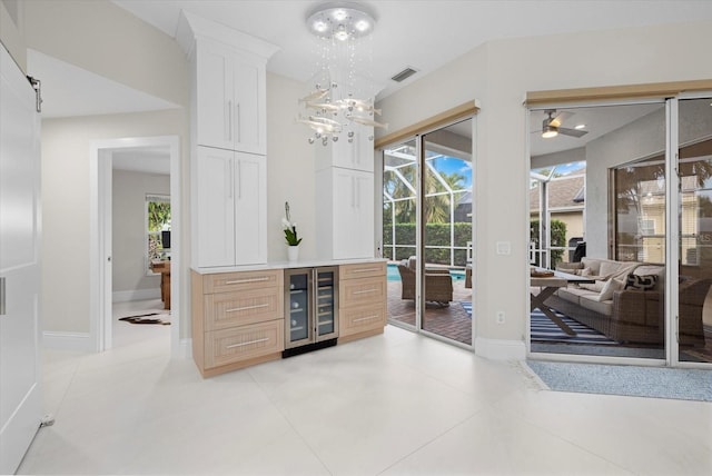 bar featuring white cabinets, ceiling fan with notable chandelier, wine cooler, light tile patterned floors, and light brown cabinetry