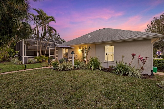 back house at dusk featuring a lanai and a yard