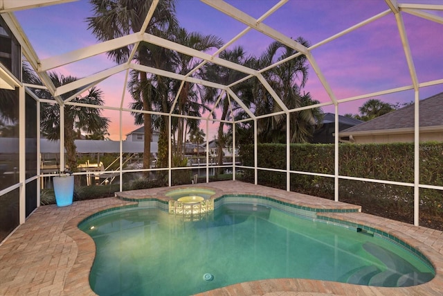 pool at dusk featuring a lanai, an in ground hot tub, and a patio