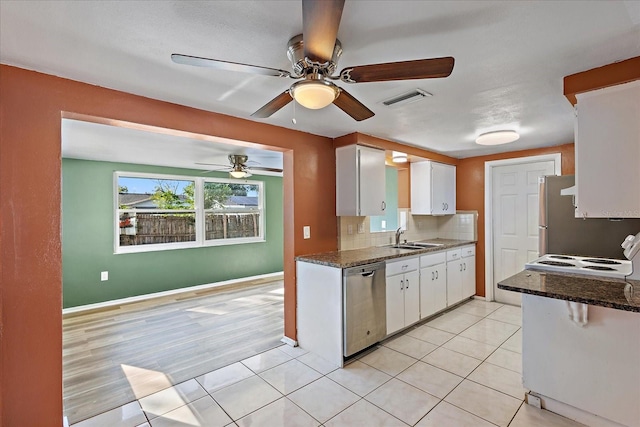 kitchen with stainless steel appliances, white cabinetry, dark stone countertops, and sink