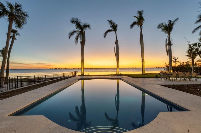 pool at dusk featuring a patio area and a water view