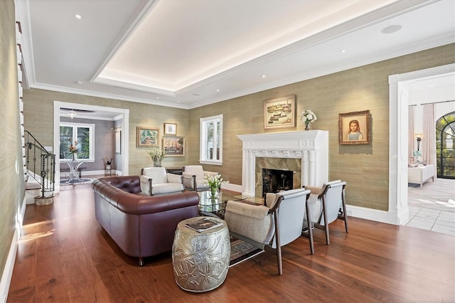 living room featuring a raised ceiling, a premium fireplace, crown molding, and hardwood / wood-style flooring