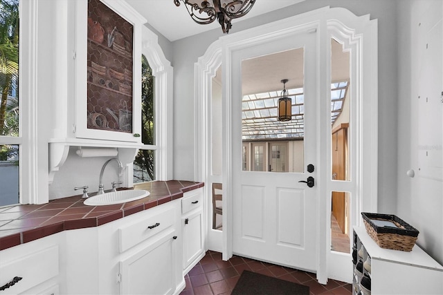 bar featuring tile countertops, white cabinets, sink, dark tile patterned floors, and a chandelier