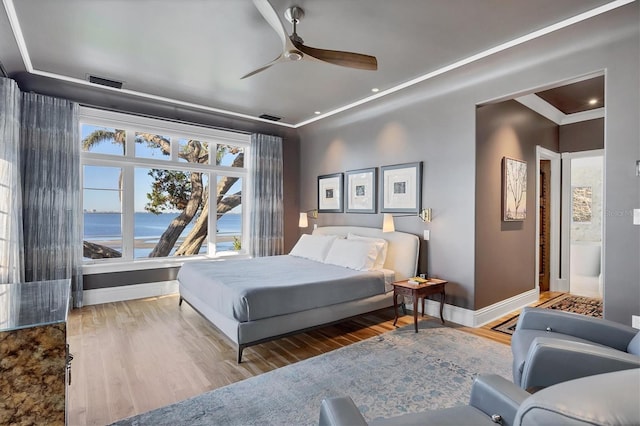 bedroom featuring wood-type flooring, a water view, ceiling fan, and crown molding