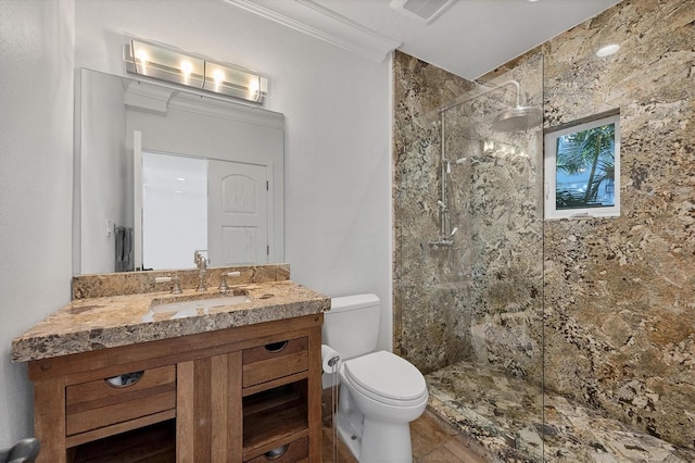 bathroom with a tile shower, crown molding, vanity, and toilet