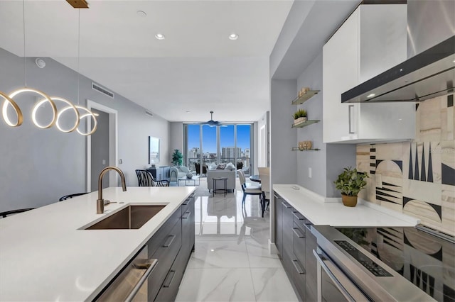 kitchen with pendant lighting, wall chimney exhaust hood, white cabinetry, and sink