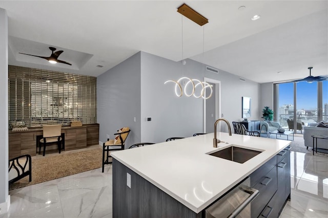 kitchen with floor to ceiling windows, ceiling fan, sink, an island with sink, and pendant lighting