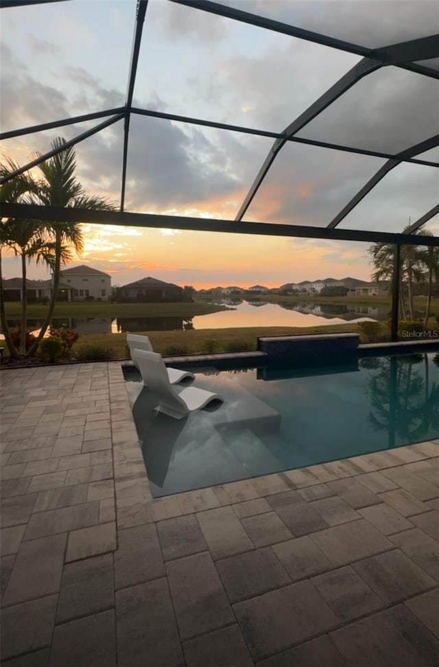 pool at dusk with a patio, a water view, and a lanai