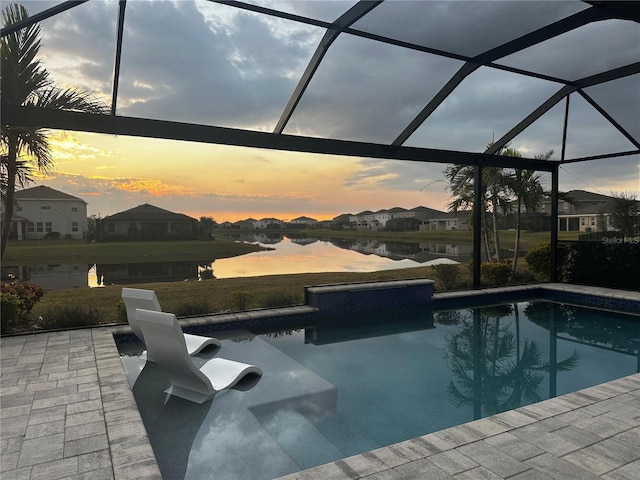 pool at dusk featuring glass enclosure, a water view, and a patio