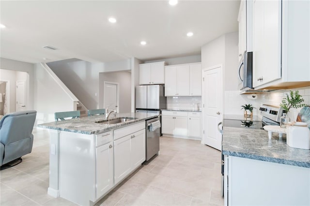 kitchen featuring backsplash, white cabinets, a center island with sink, sink, and stainless steel appliances