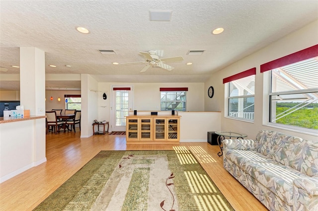 living room featuring ceiling fan, a textured ceiling, and light wood-type flooring