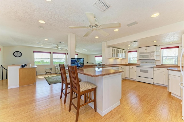 kitchen with white appliances, a kitchen breakfast bar, kitchen peninsula, a textured ceiling, and white cabinetry