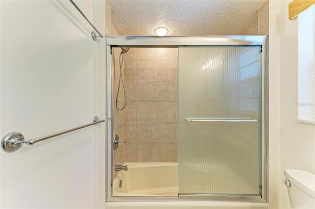 bathroom with bath / shower combo with glass door, a textured ceiling, and toilet