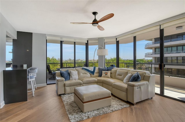 living room with light wood-type flooring, a wall of windows, plenty of natural light, and ceiling fan