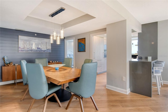 dining area featuring a chandelier, a tray ceiling, light hardwood / wood-style flooring, and wood walls