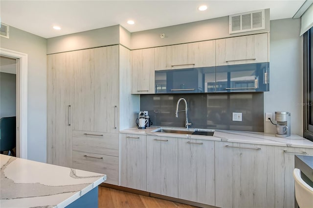 kitchen with tasteful backsplash, light stone countertops, sink, and light hardwood / wood-style flooring