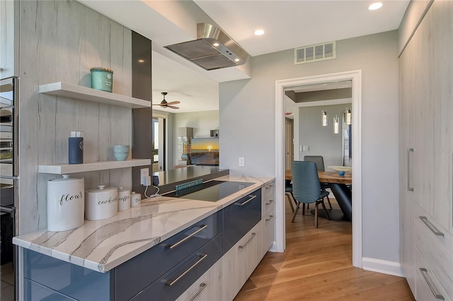 kitchen with light stone countertops, island range hood, ceiling fan, electric stovetop, and light hardwood / wood-style flooring