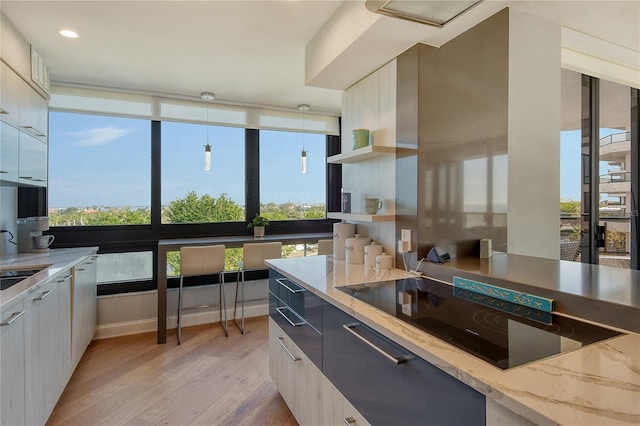 kitchen featuring black electric stovetop, light stone counters, sink, pendant lighting, and light hardwood / wood-style floors