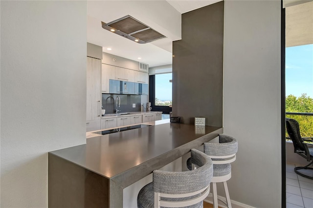 kitchen with sink, kitchen peninsula, stovetop, a breakfast bar, and light tile patterned floors