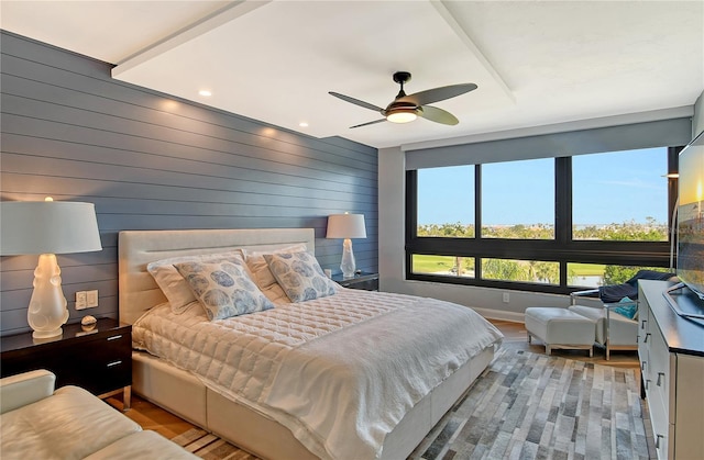 bedroom featuring ceiling fan, light hardwood / wood-style floors, and wooden walls