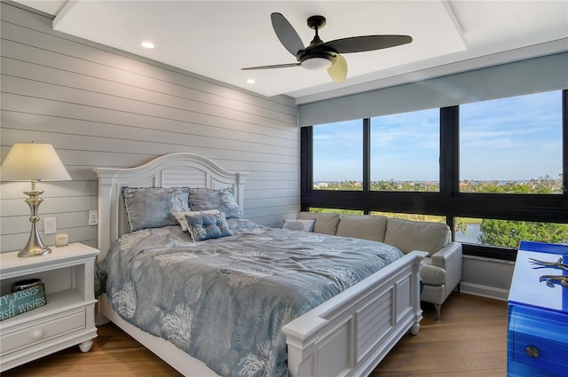 bedroom featuring hardwood / wood-style floors, ceiling fan, and wood walls