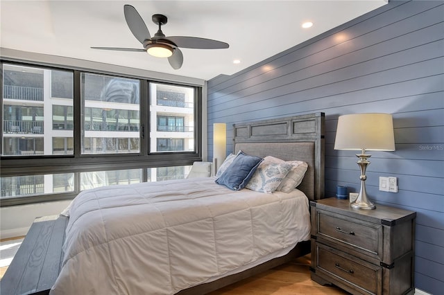 bedroom with light hardwood / wood-style floors, ceiling fan, and wood walls