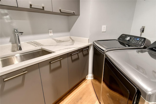 clothes washing area featuring washer and dryer, sink, cabinets, and light hardwood / wood-style floors