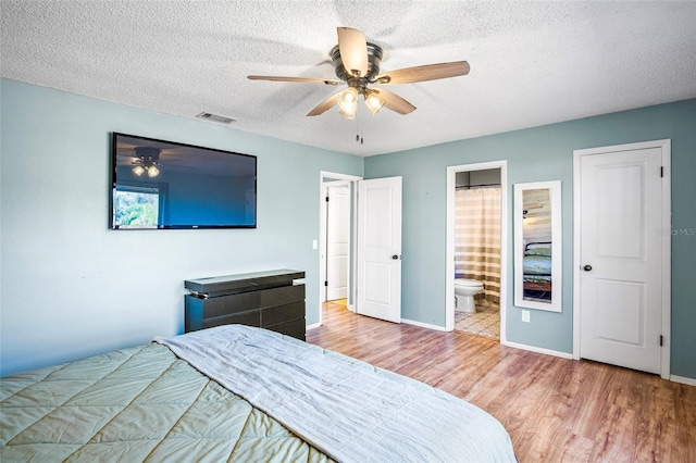 bedroom with ceiling fan, connected bathroom, a textured ceiling, and light wood-type flooring