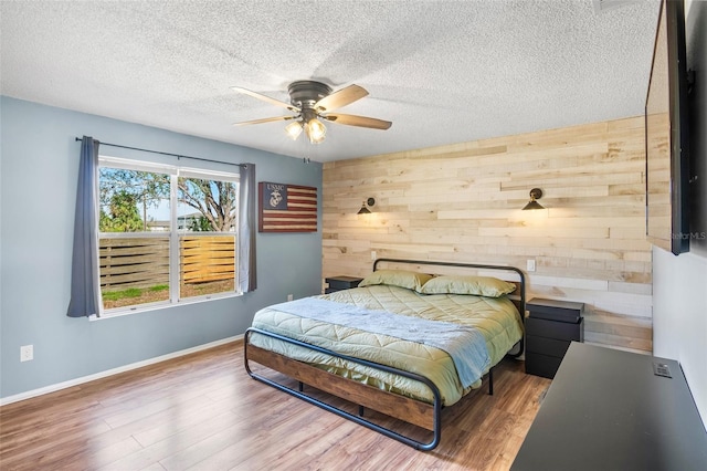 bedroom with wood-type flooring, a textured ceiling, wooden walls, and ceiling fan