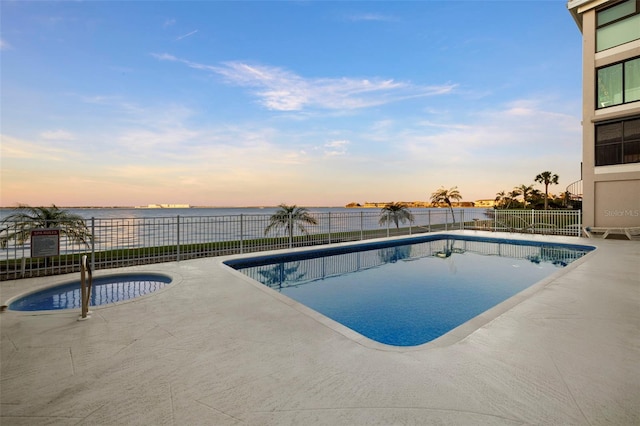 pool at dusk with a patio area, a hot tub, and a water view