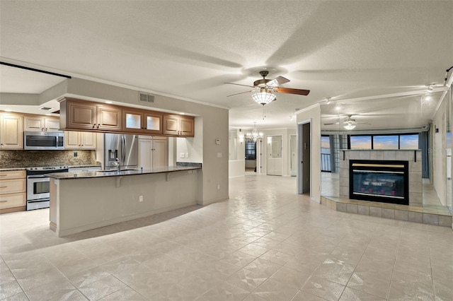 kitchen with a kitchen bar, an inviting chandelier, a tiled fireplace, stainless steel appliances, and ornamental molding