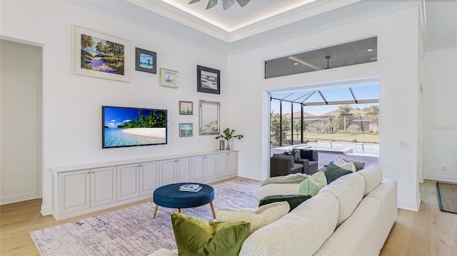 living room featuring a towering ceiling, light hardwood / wood-style flooring, ornamental molding, and ceiling fan