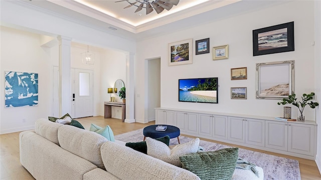 living room with ornate columns, a raised ceiling, ceiling fan, and light wood-type flooring