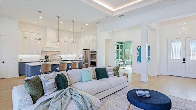 living room featuring decorative columns, ornamental molding, a chandelier, and light hardwood / wood-style flooring