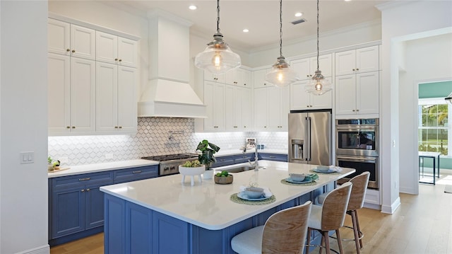 kitchen with blue cabinetry, stainless steel appliances, an island with sink, and premium range hood