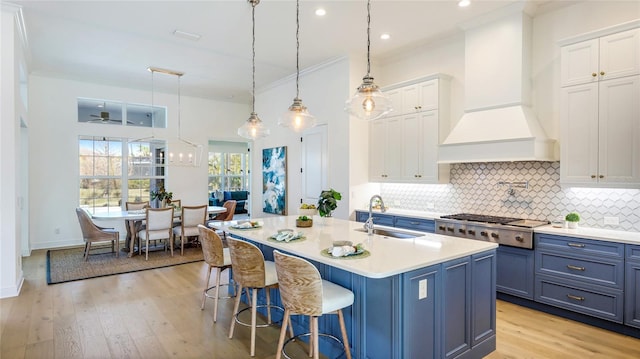 kitchen with sink, white cabinetry, decorative light fixtures, an island with sink, and custom range hood