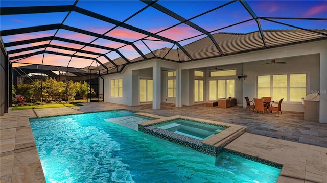 pool at dusk with an in ground hot tub, ceiling fan, a lanai, and a patio