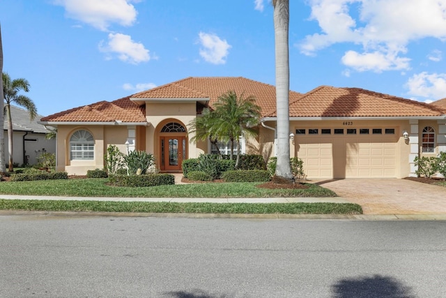 mediterranean / spanish house with an attached garage, driveway, a tile roof, and stucco siding