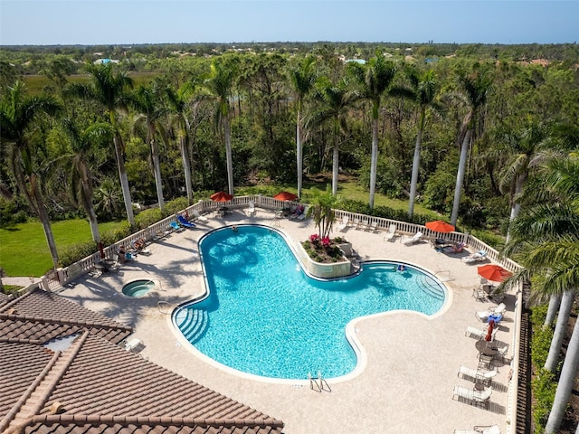 pool with a community hot tub, a patio, a view of trees, and fence